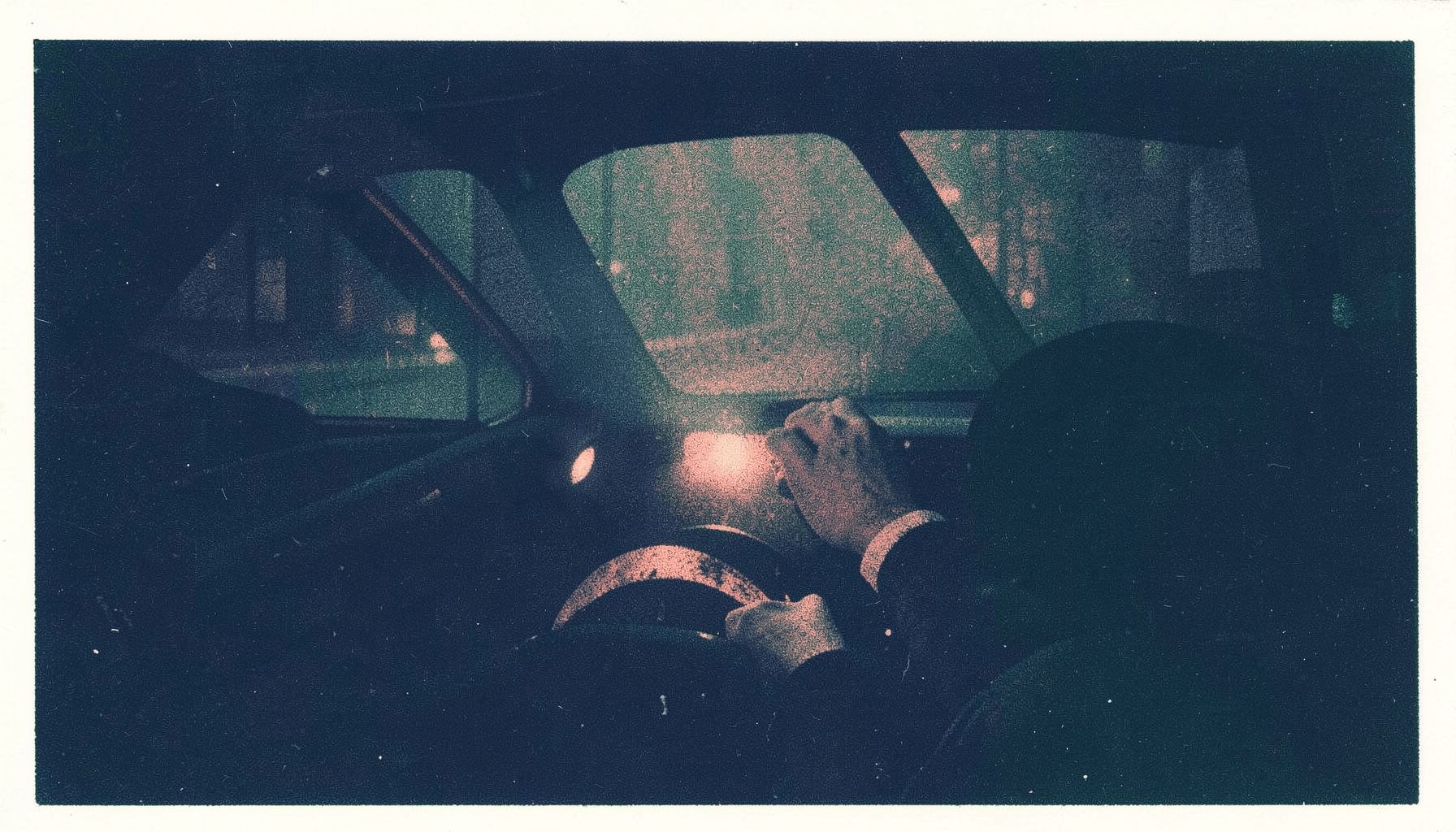 A dark risograph composition in navy and muted coral of a car interior at night, a driver's hands gripping the wheel, headlights cutting through fog ahead.